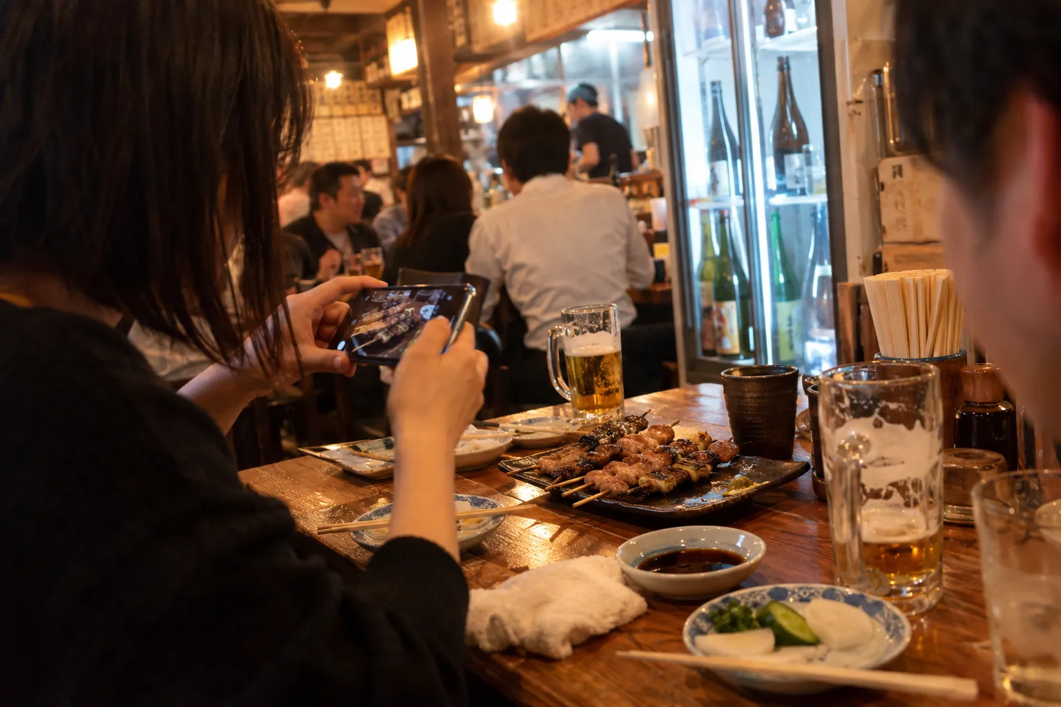 居酒屋でお客さんが焼き鳥をスマホで撮っている
